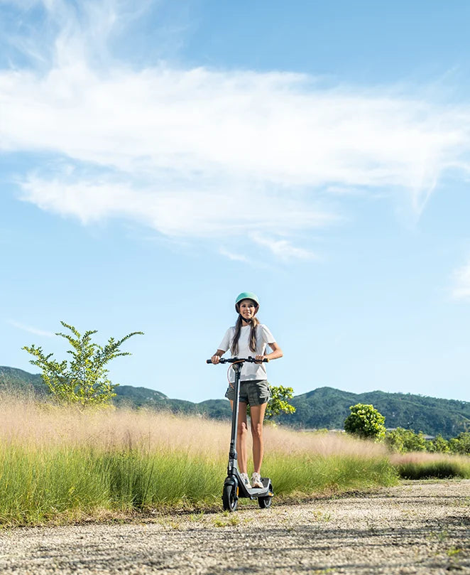 Female rider on CUNFON RS300 electric scooter cruising through scenic park pathway, representing sustainable urban mobility with 500W motor, 30KM/H speed, and IP56 waterproof smart design.